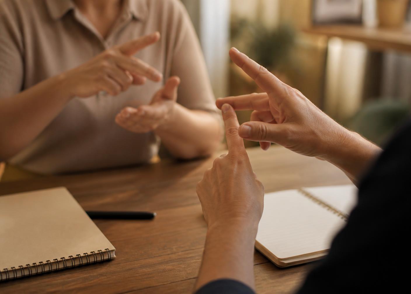 Two learners practising British Sign Language across a table